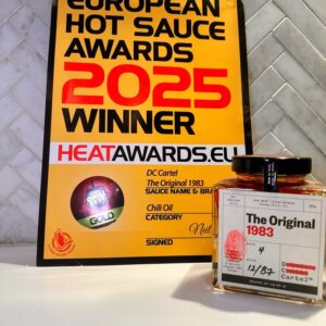 Chiliöl mit Sonnenblumenöl und Ein Zertifikat der European Hot Sauce Awards 2025, das DC CARTEL The Original 1983 als Gewinner in der Kategorie Chiliöl auszeichnet. Daneben steht die preisgekrönte Glasflasche mit dem markanten roten Fingerabdruck.