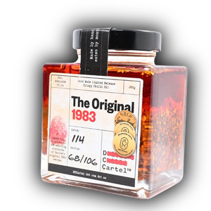 Seitenansicht der DC CARTEL Chiliöl Flasche in der Produktgalerie. Man sieht deutlich die Schichtung der Chiliflocken im Öl und die goldenen Award-Siegel auf der Vorderseite.