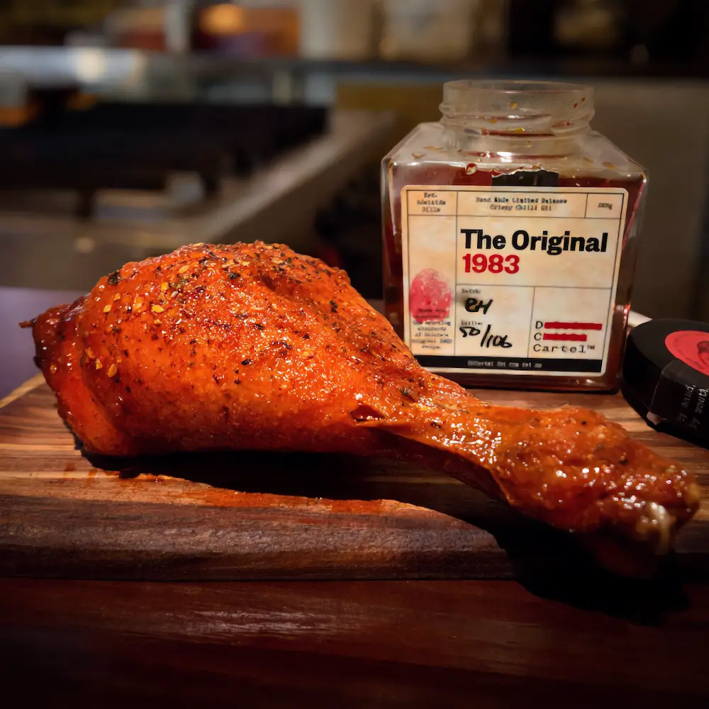 Knusprig gegrillte Hähnchenkeule mit DC CARTEL Crispy Chiliöl Kruste auf einem Holzbrett